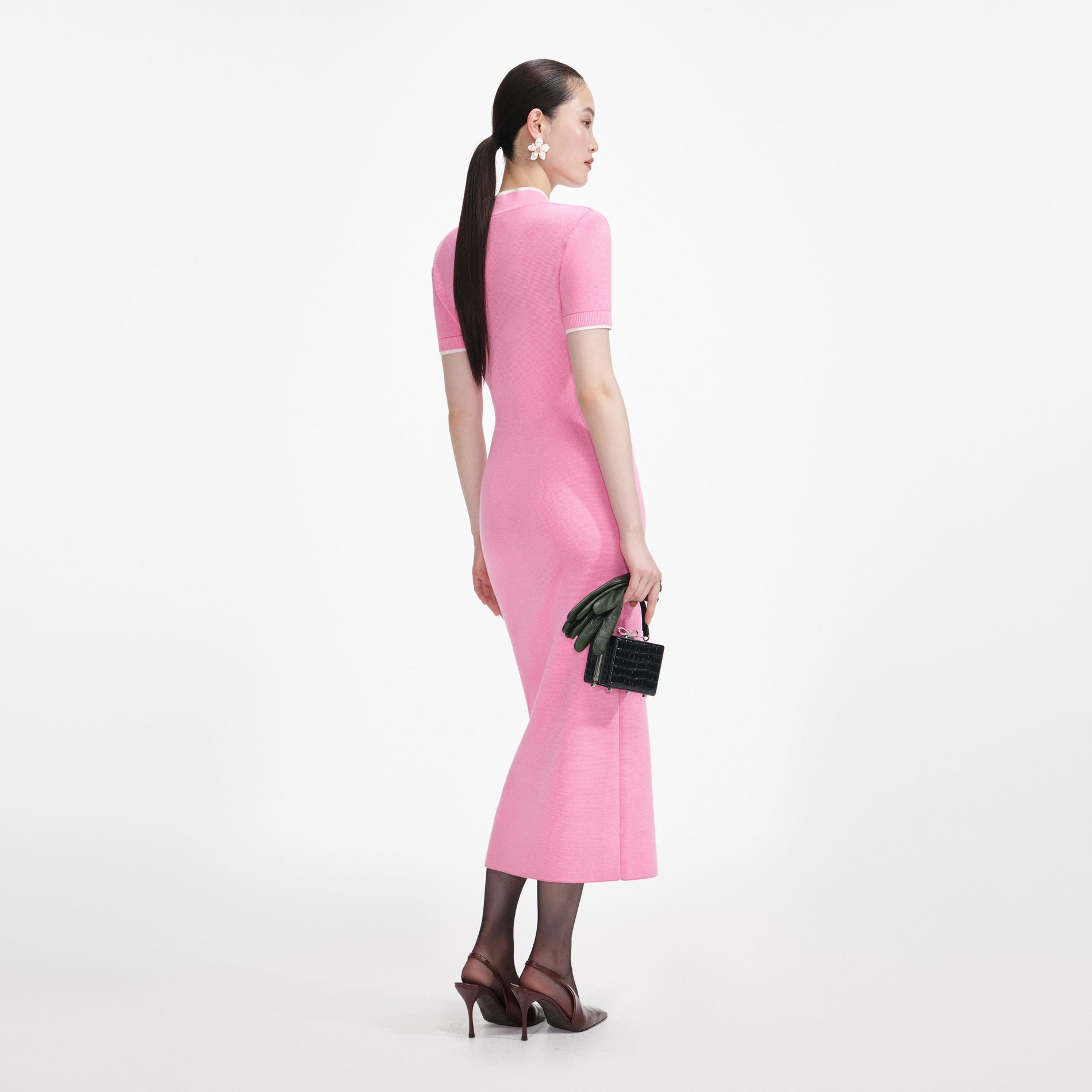 Woman in pink dress, dark green gloves, and black handbag, facing away from the camera