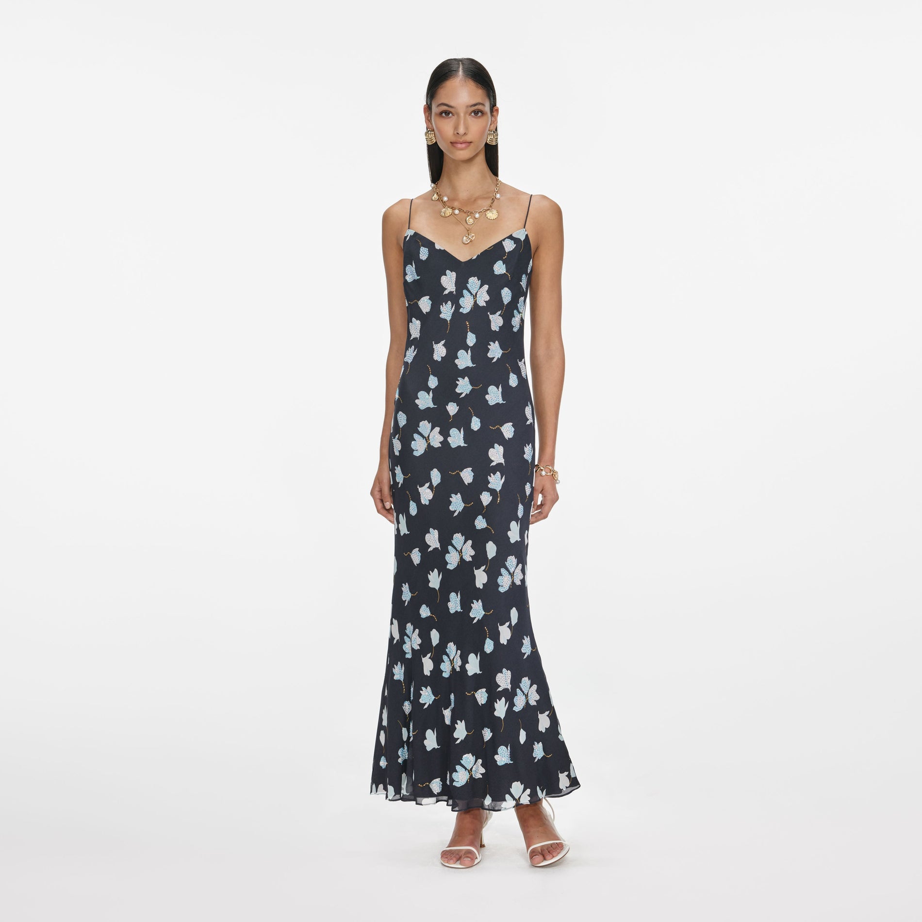 Woman in a black floral maxi dress with thin straps, gold earrings, and a gold necklace with shell charms