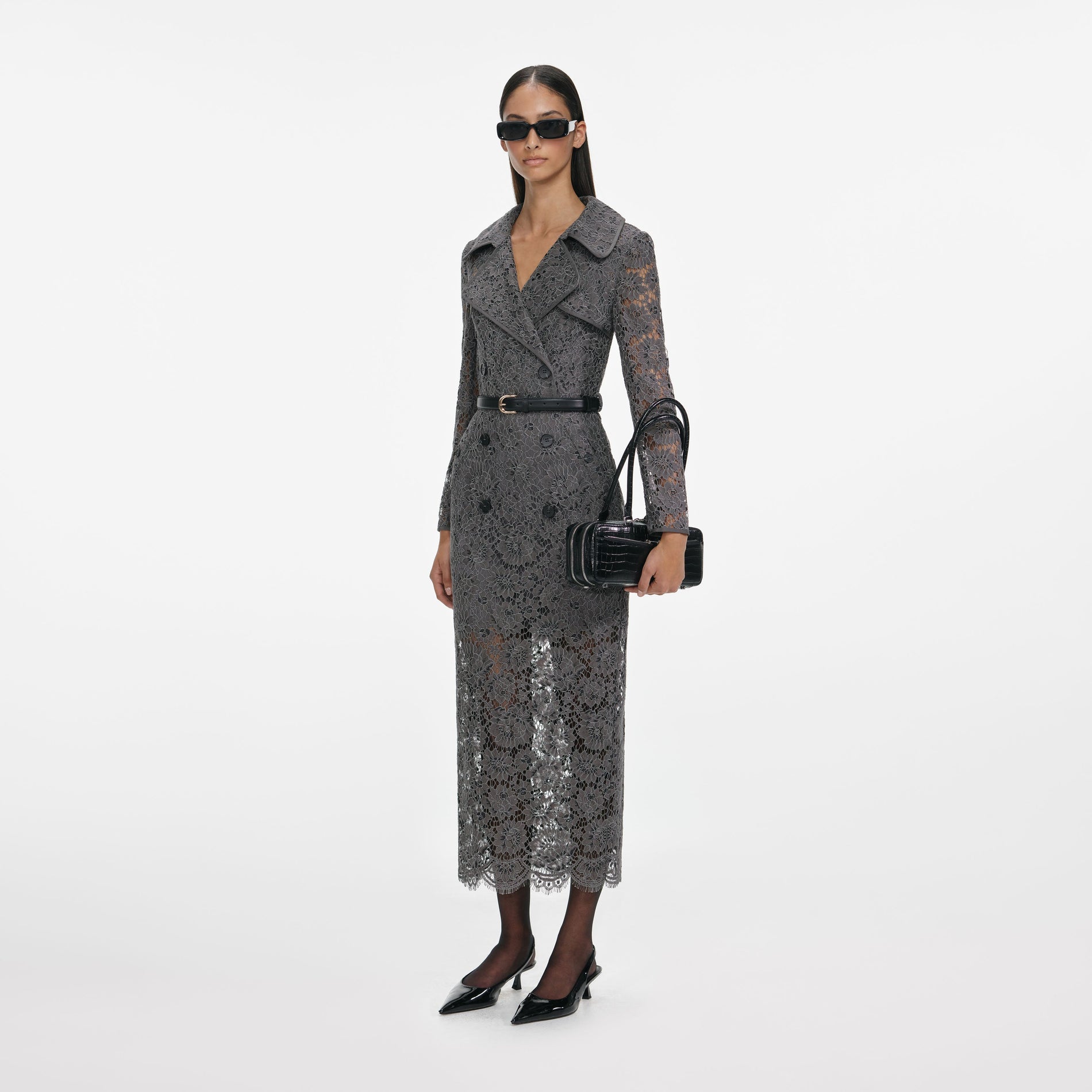Woman wearing a grey lace trench coat with a black belt, black sunglasses, and black slingback heels