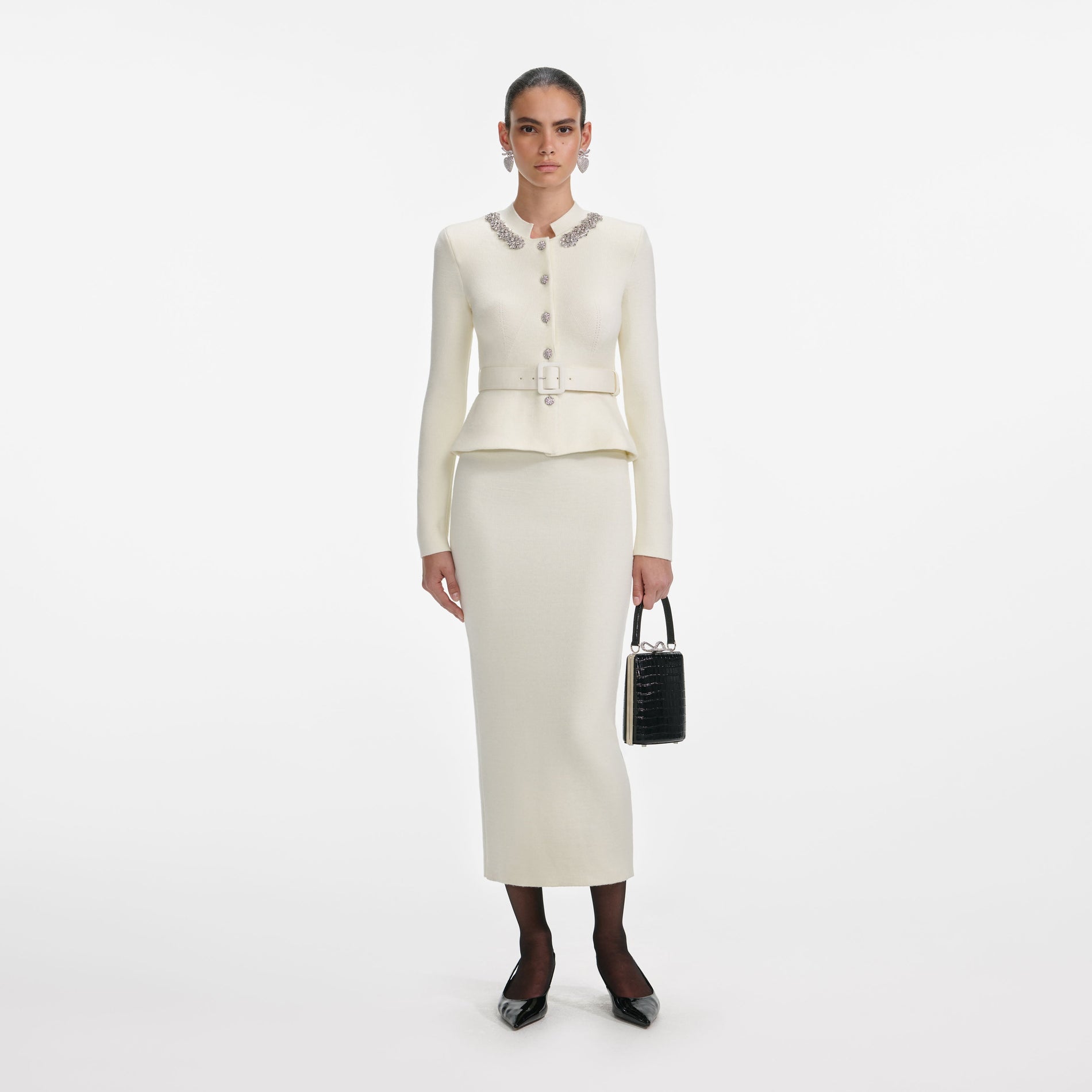 Woman in a cream knit peplum jacket with a belted waist and a matching midi skirt
