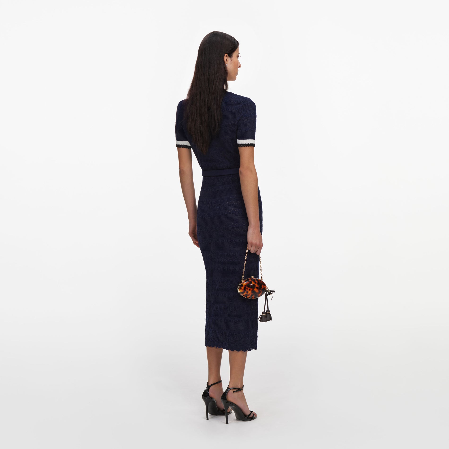 Woman in navy blue short-sleeve knit dress with white and black striped cuffs, holding a tortoiseshell clutch
