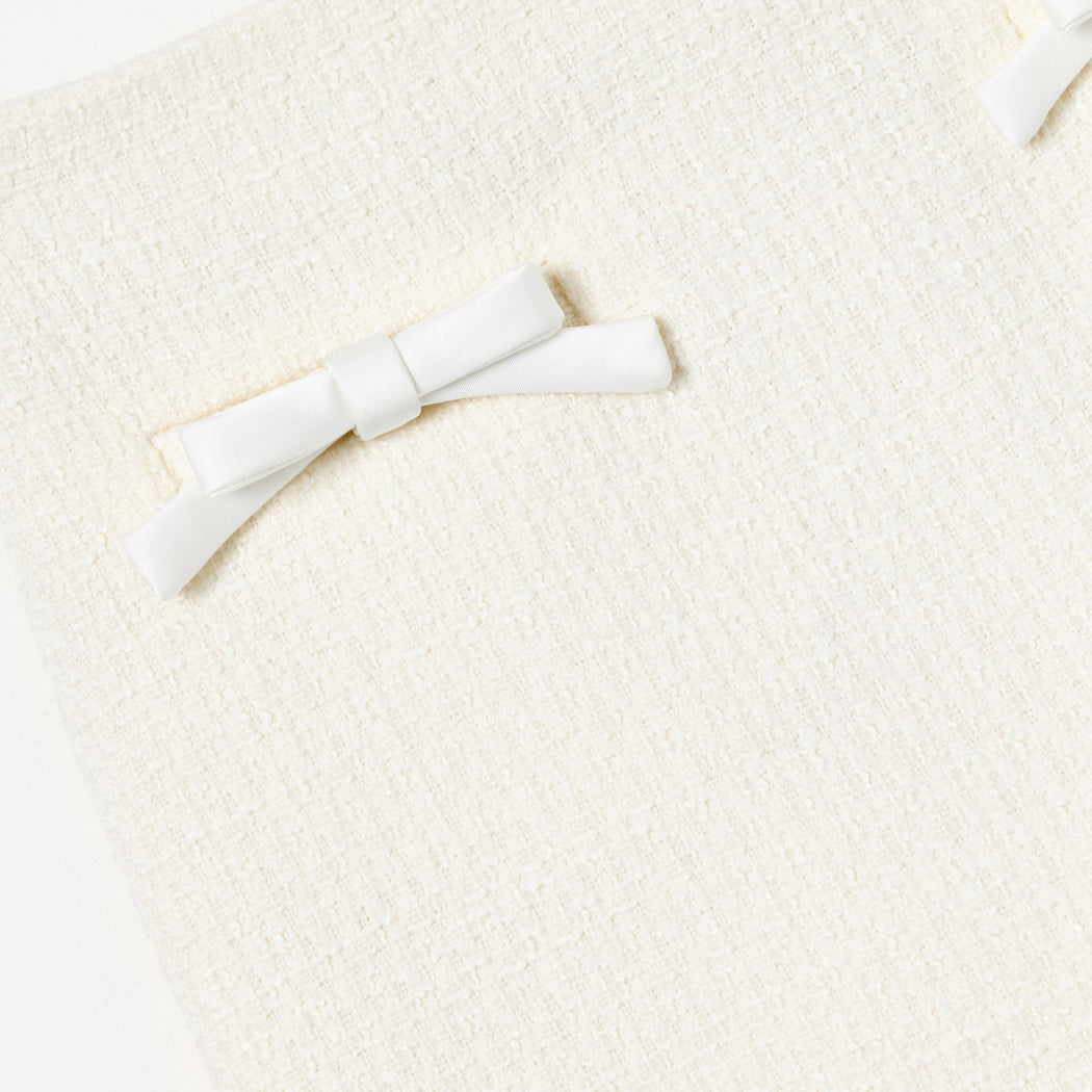 Close up of cream tweed fabric with two white satin bows