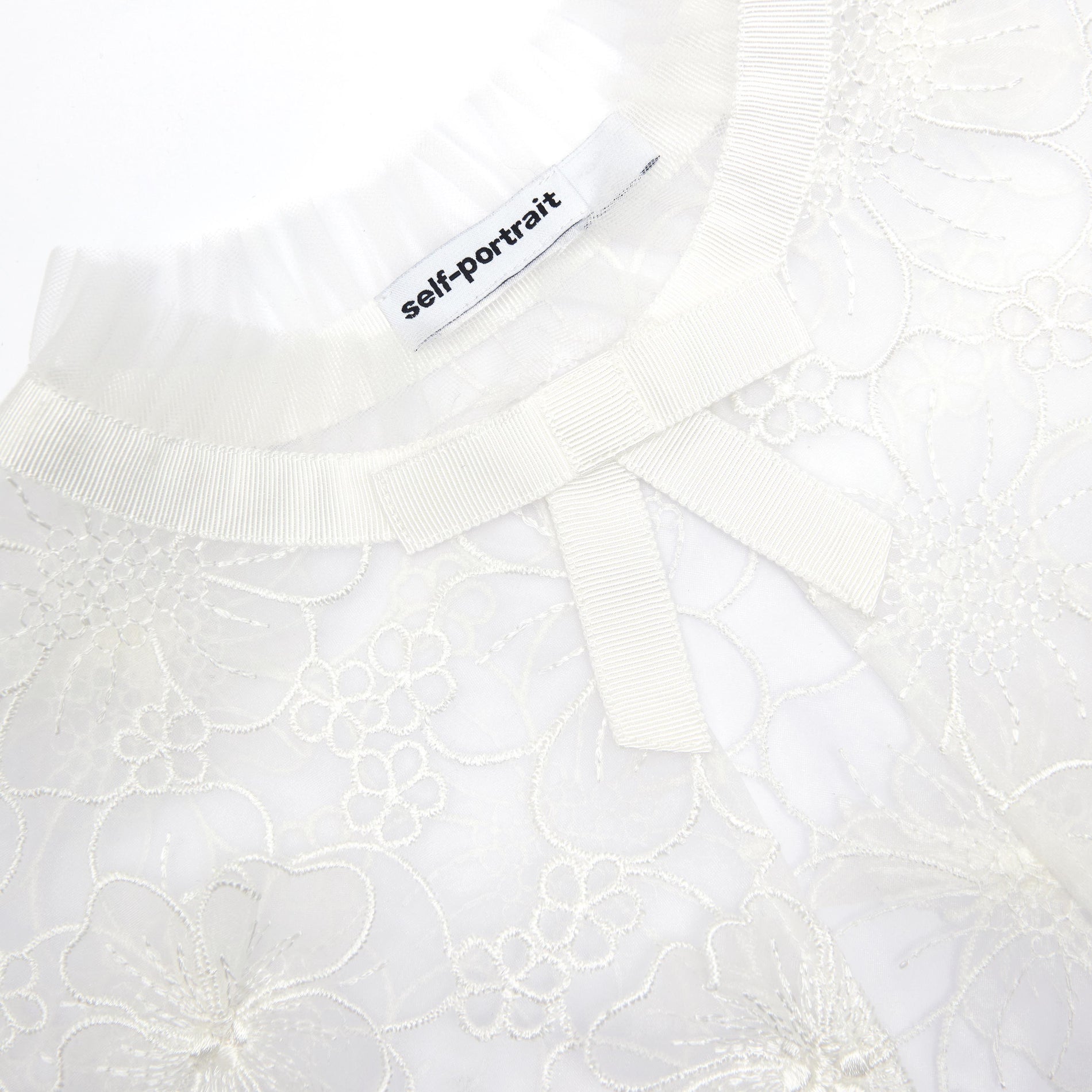 Self-Portrait brand tag on a white lace top with a bow