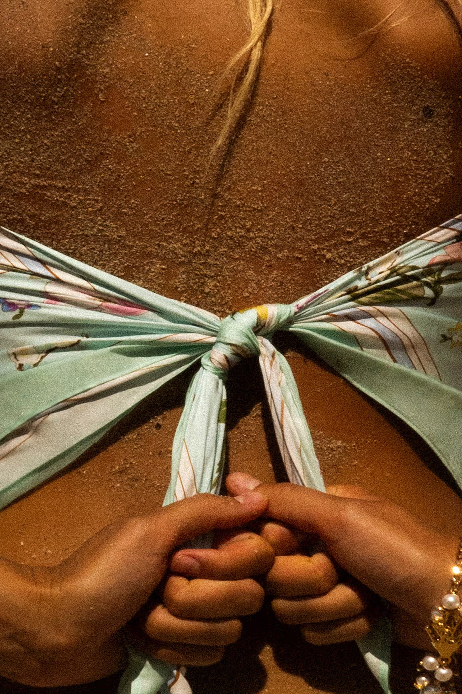 Close-up of hands tying a floral mint scarf.