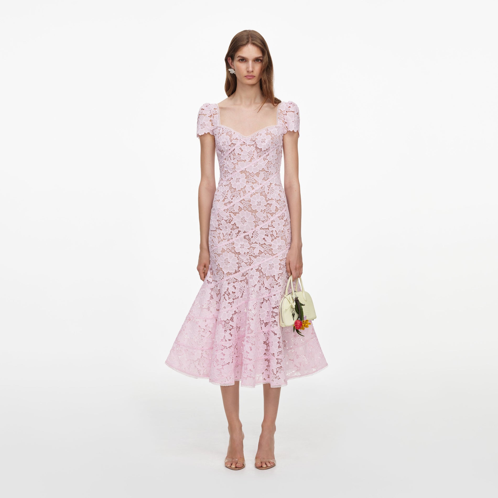 Woman in a pink lace midi dress with short sleeves and a sweetheart neckline, holding a small white handbag