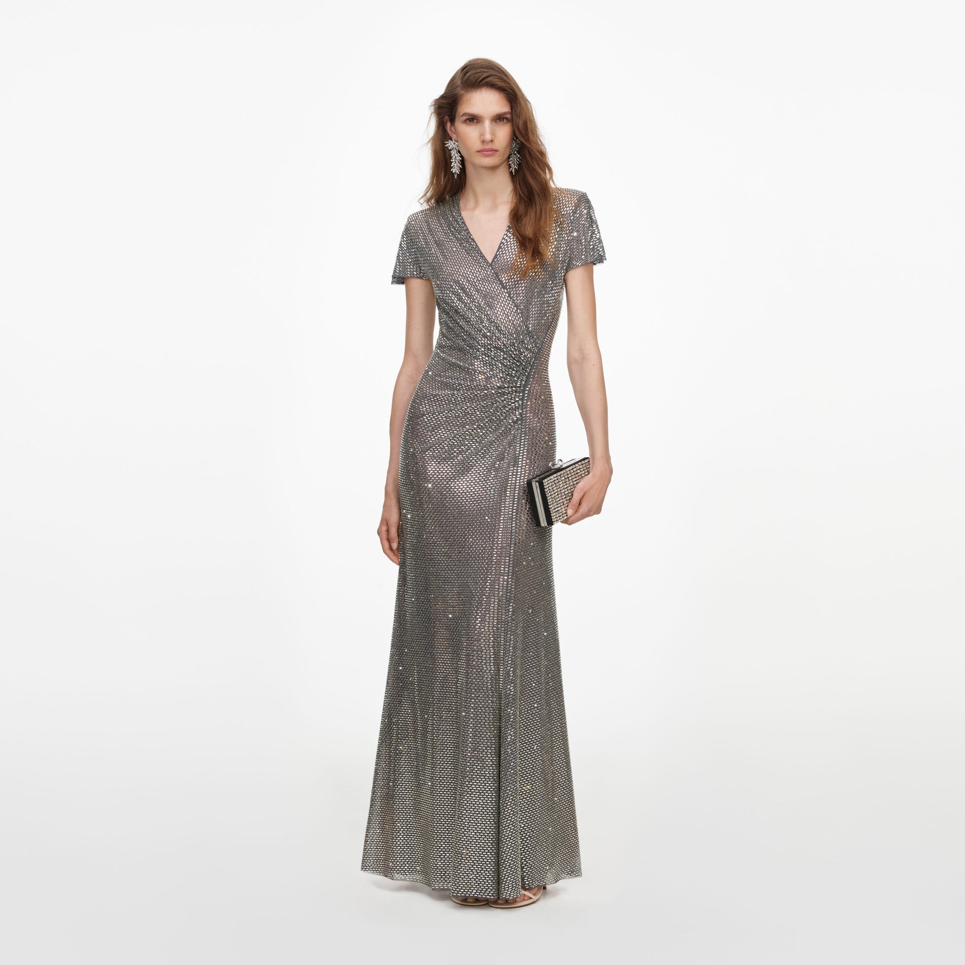 Woman in a silver sequin maxi dress with short sleeves, a v-neck, and a ruched waist, holding a clutch