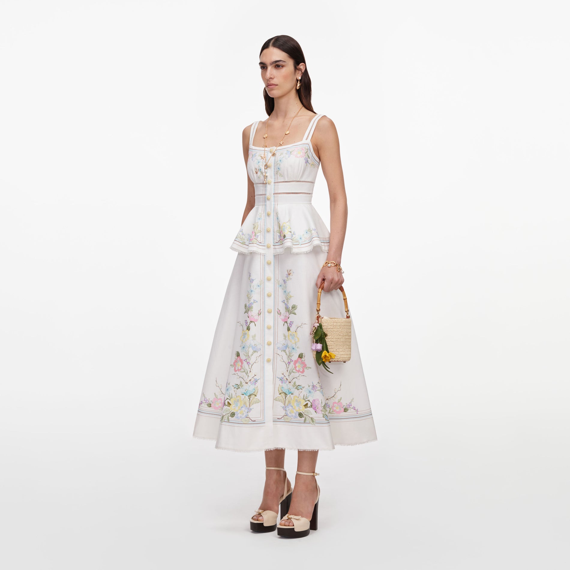 Woman in white floral embroidered dress with straw bag and platform heels