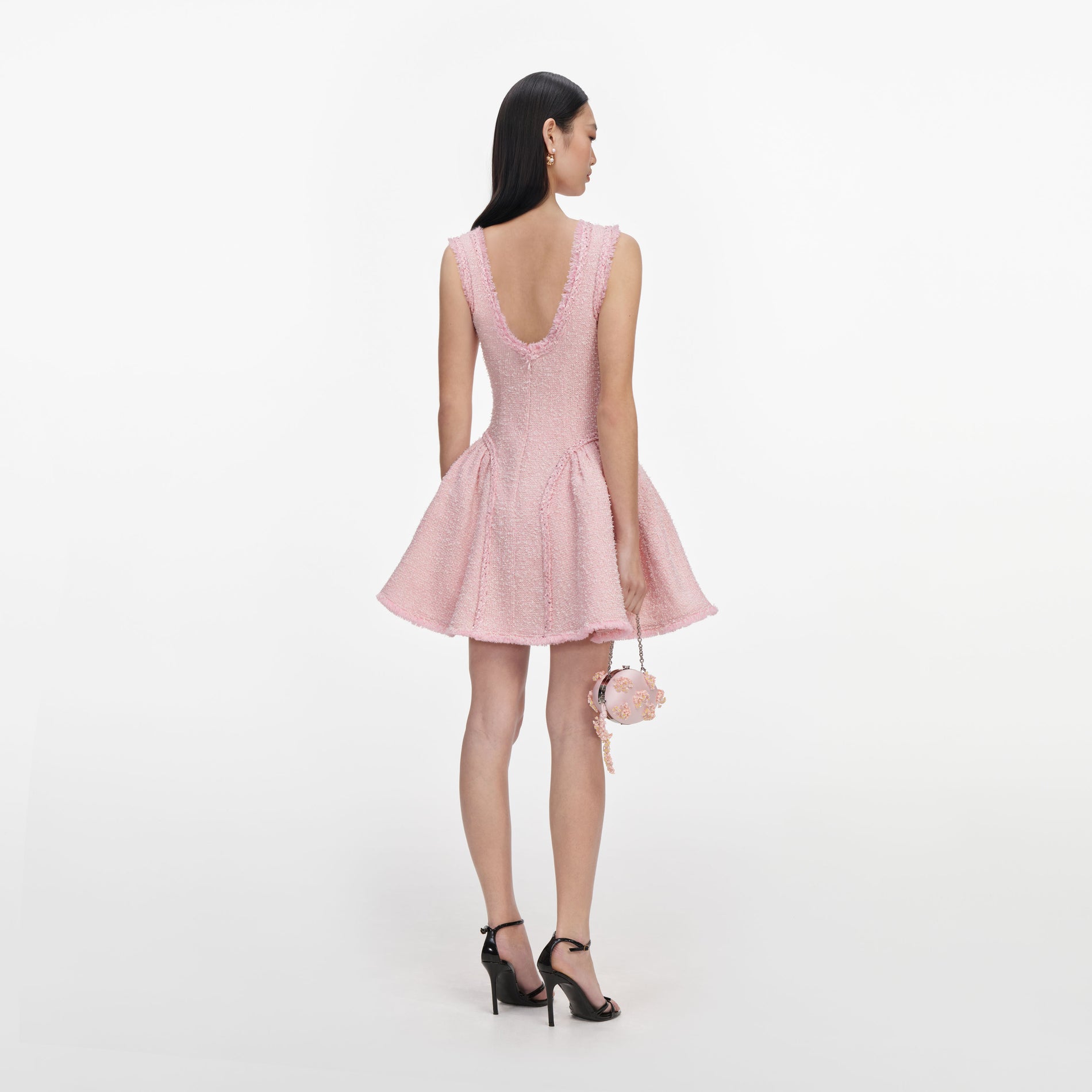 Woman in pink tweed mini dress with a scoop neck and flared skirt, holding a small round pink purse
