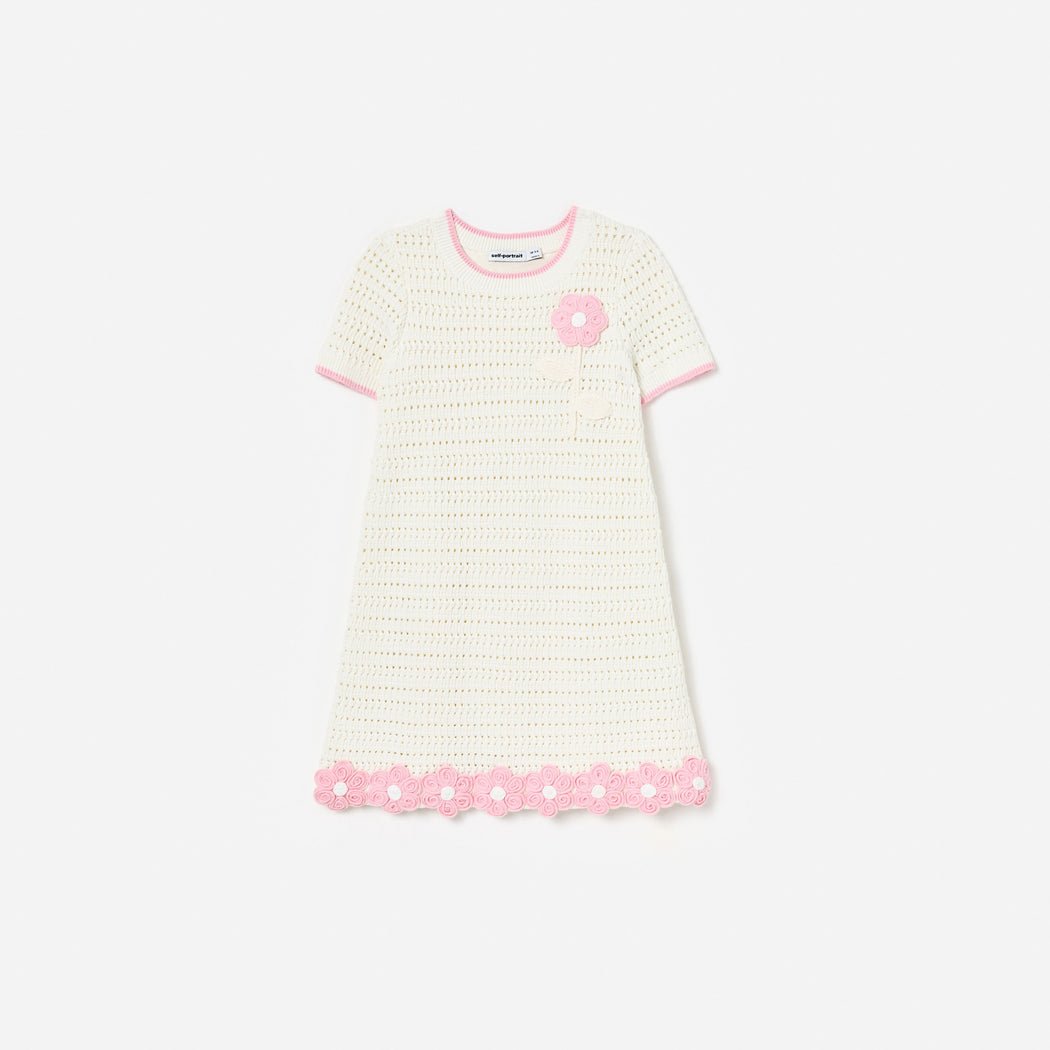 White crochet dress with pink trim, a pink flower applique on the chest, and pink floral details on the hem