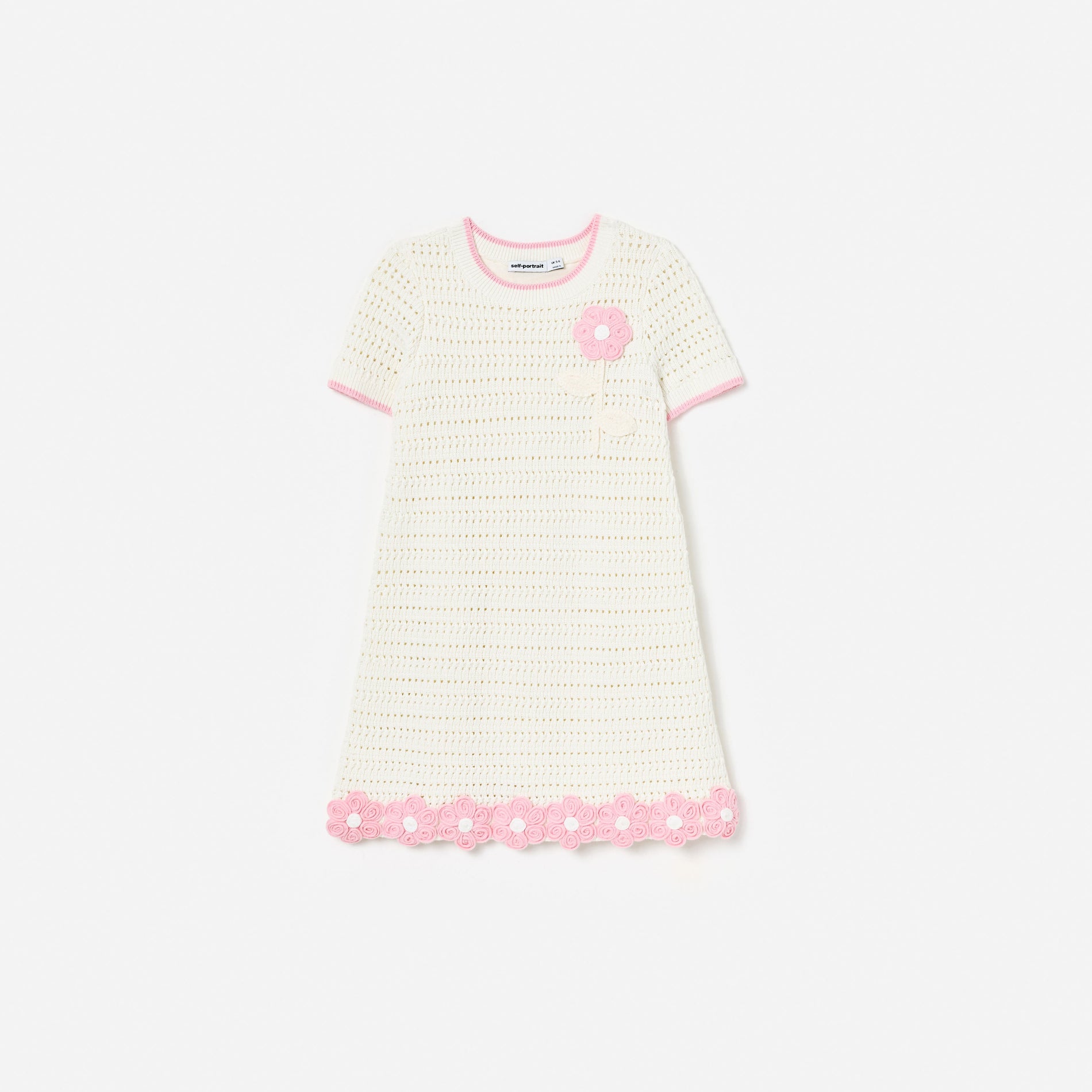 White crochet dress with pink trim, a pink flower applique on the chest, and pink floral details on the hem