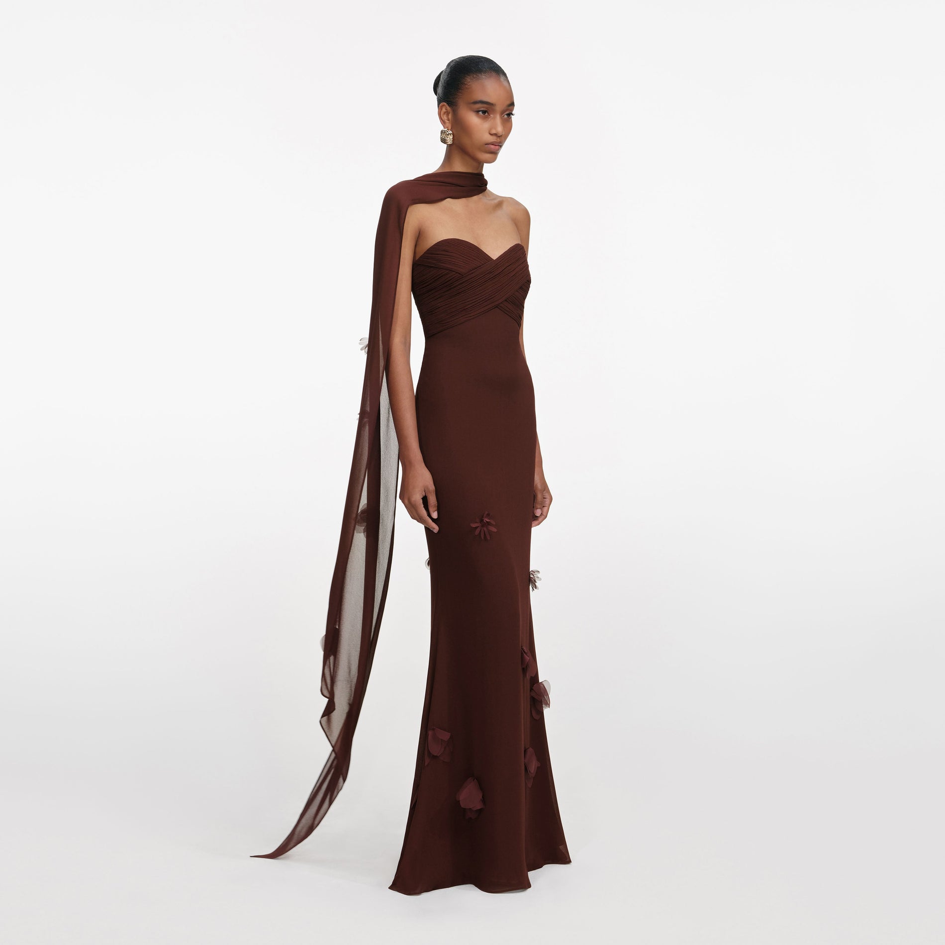 Model wearing a brown strapless gown with a flowing sheer sleeve and floral appliques